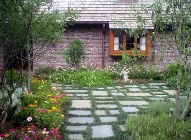 Bluestone stepping stones in groundcover with zinnias and perennials beside a brick cottage