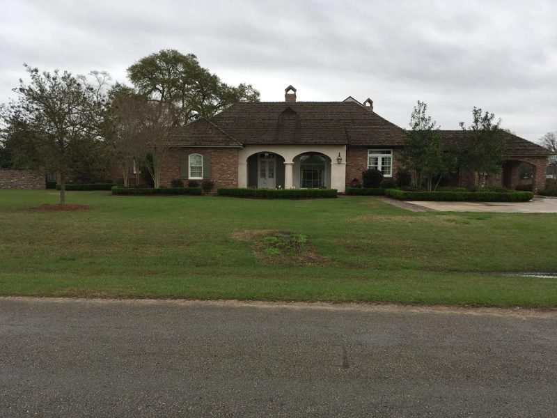 Brick home with an arched entry, low clipped hedge lines and a wide lawn