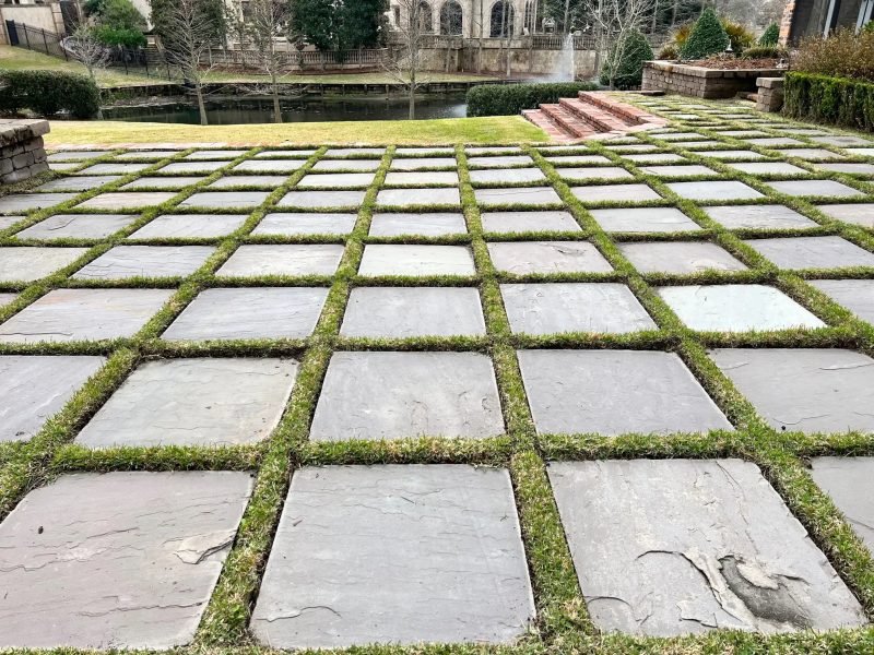 Large slate pavers with grass joints leading to a lawn and a pond with a fountain