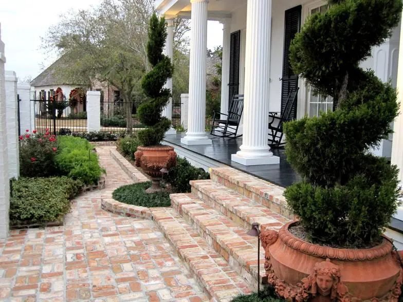 Columned porch with spiral topiaries in terracotta urns and brick steps