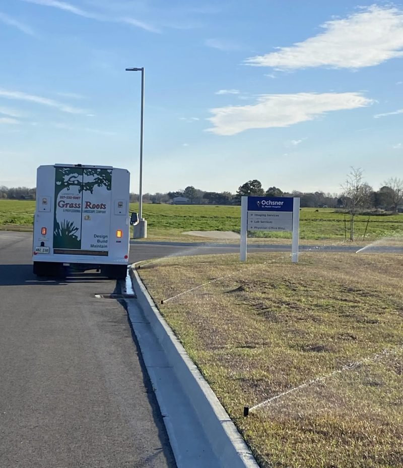 Grass Roots service truck parked by rotor sprinklers watering a roadside lawn