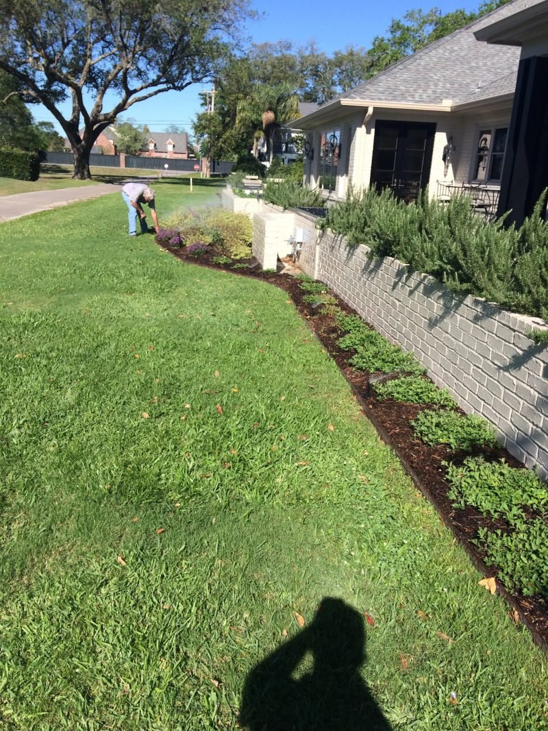 Technician adjusting a sprinkler head along a curved bed beside a home