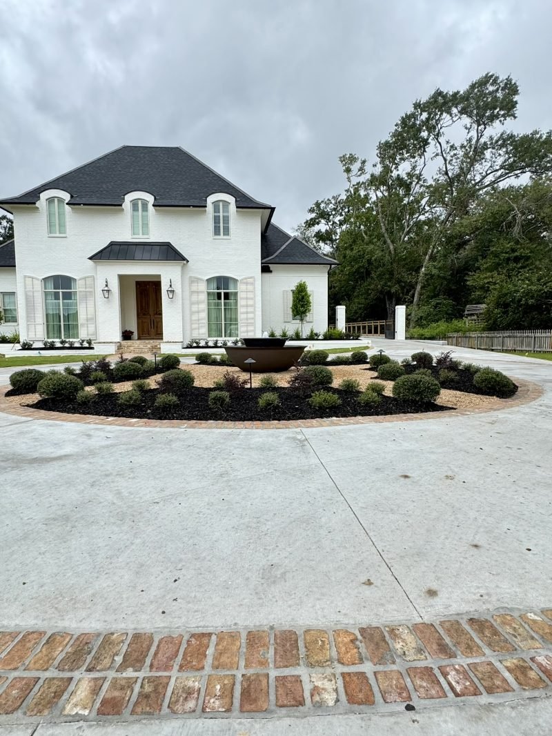 White French-style home with a circular drive island of boxwoods around a fire bowl and a brick paver apron