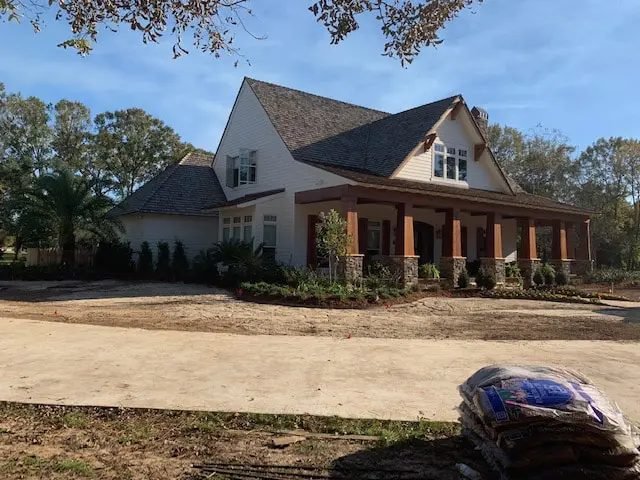 New home with a stone-column porch and freshly planted foundation beds, mulch bags in the foreground