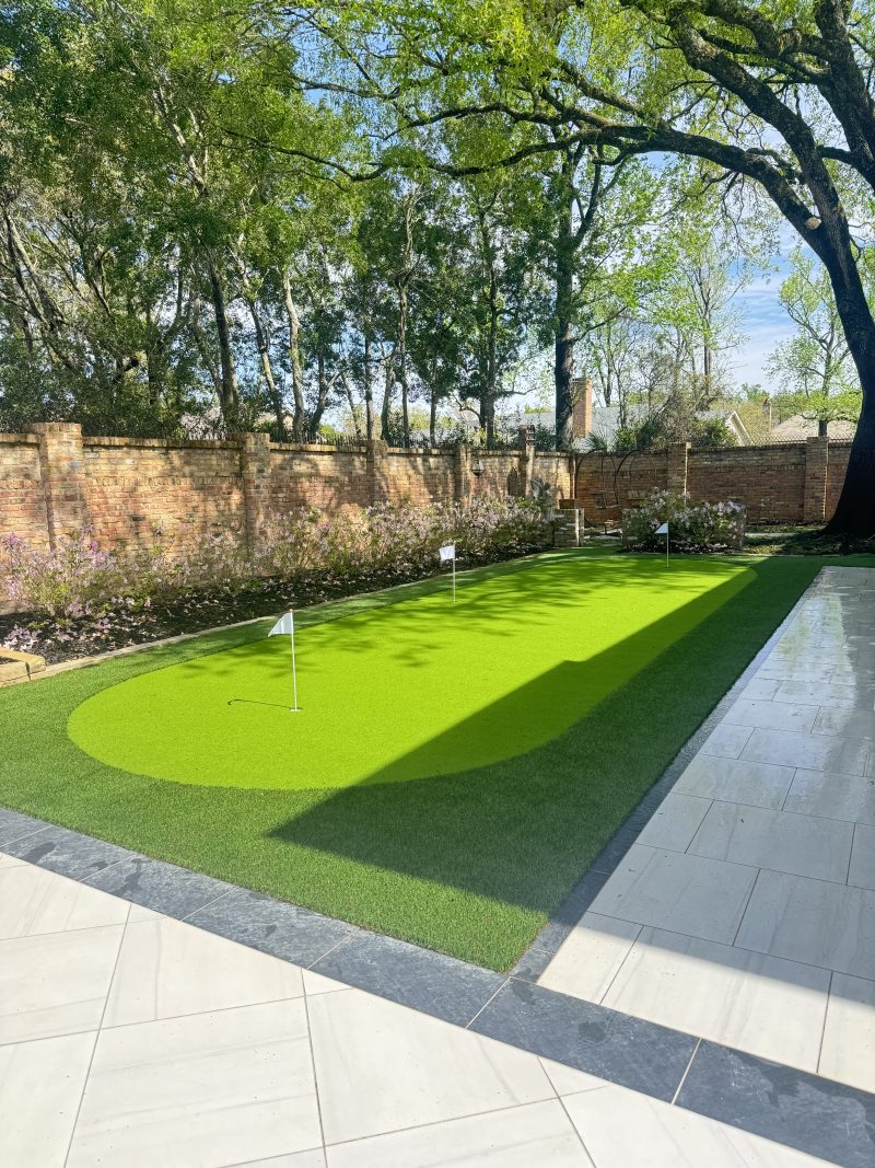 Artificial turf putting green beside a tile patio inside a brick garden wall