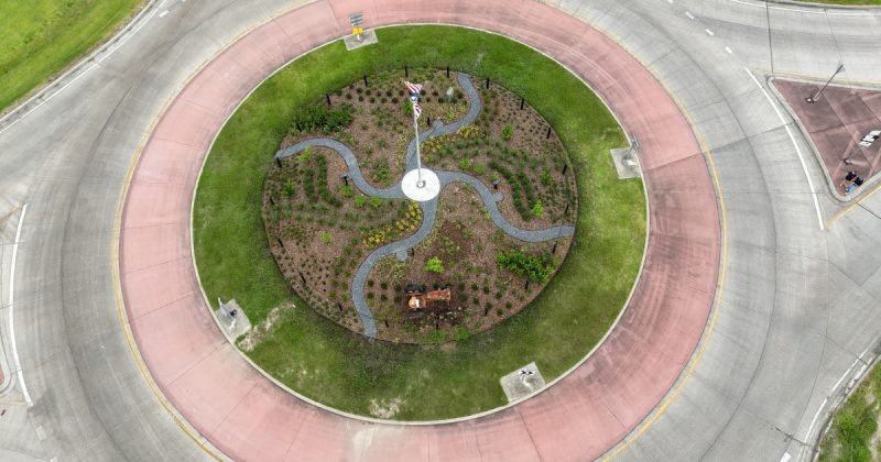 Overhead drone view of the planted roundabout island with curving paths around a flagpole