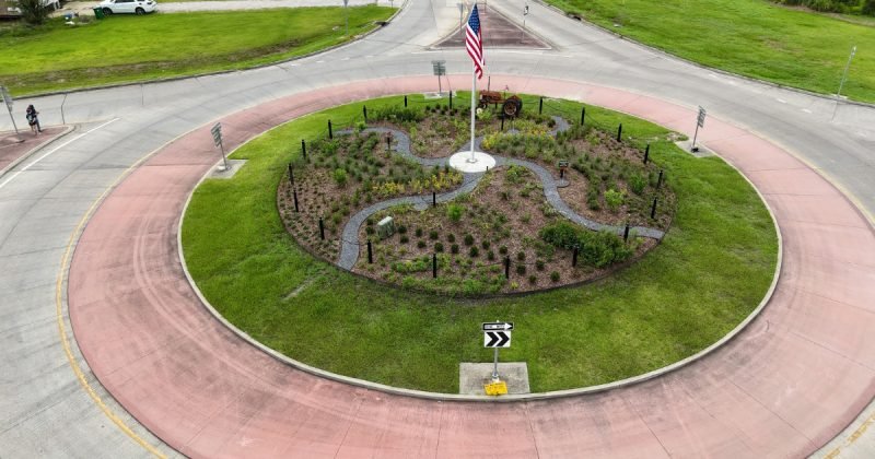 Aerial view of a roundabout island planted in a swirl of grasses and shrubs around a flagpole