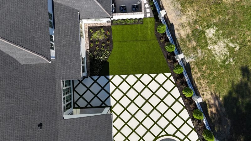 Overhead view of a side yard with a turf lawn, diamond-pattern pavers with turf joints and a row of round shrubs